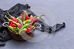 Top view of the green and red hot chili peppers in a rusty cup with cloth on a dark tabletop