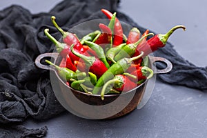 Top view of the green and red hot chili peppers in a rusty cup with cloth on a dark tabletop