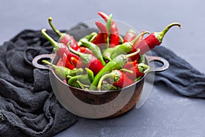 Top view of the green and red hot chili peppers in a rusty cup with cloth on a dark tabletop