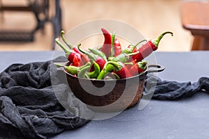 Top view of the green and red hot chili peppers in a rusty cup with cloth on a dark tabletop