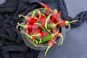 Top view of the green and red hot chili peppers in a rusty cup with cloth on a dark tabletop