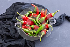 Top view of the green and red hot chili peppers in a rusty cup with cloth on a dark tabletop