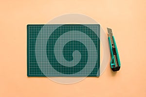 Top view of green rubber cutting mat with green cutter over pale orange color paper background. Background with copy space