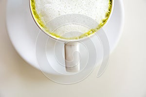 Top view of green tea foam matcha latte with the saucer on white table background. Hot milk green tea (selective focus)