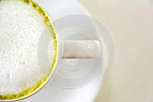 Top view of green tea foam matcha latte with the saucer on white table background. Hot milk green tea (selective focus)