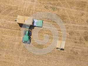 Top view of green tractor loading straw bales on a trailer