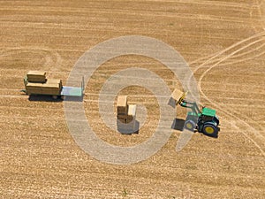 Top view of green tractor loading straw bales on a trailer