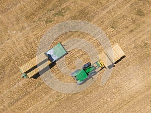 Top view of green tractor loading straw bales on a trailer