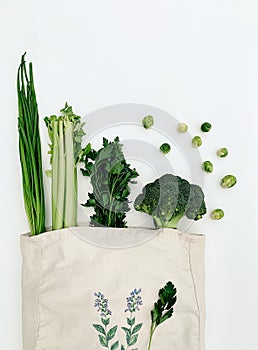 Top view of green vegetables in an eco cotton tote bag on a white background.