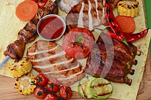 Top view of grilled meal of steak and vegetables spread out on rustic wooden board over bright green background