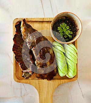 Top view of Grilled pork ribs, sliced cucumber and spicy sauce on wooden tray.