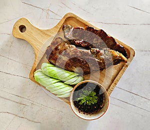 Top view of Grilled pork ribs, sliced cucumber and spicy sauce on wooden tray.