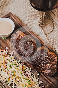 Top view grilled ribeye beef steak with stew cabbage and wineglass of red wine, herbs and spices over brown sackcloth on