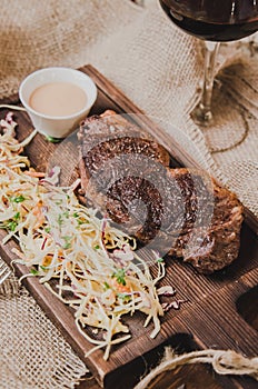 Top view grilled ribeye beef steak with stew cabbage and wineglass of red wine, herbs and spices over brown sackcloth on