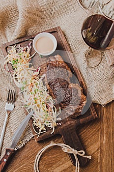 Top view grilled ribeye beef steak with stew cabbage and wineglass of red wine, herbs and spices over brown sackcloth on