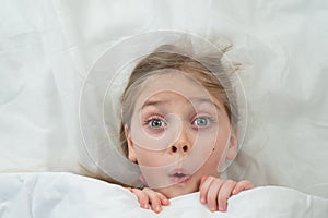 Top view of a grimacing little girl lying in bed.