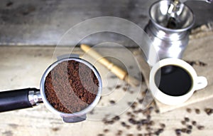 Top view ground coffee in a basket of the portafilter with blur background of rustic wooden table cup of black coffee and roasted