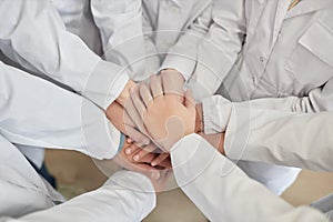 Top view of group of children stacking hands in science class white lab coats