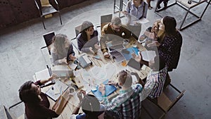 Top view of group of mixed race people sitting at table, talking and then start to clapping together. Business meeting.