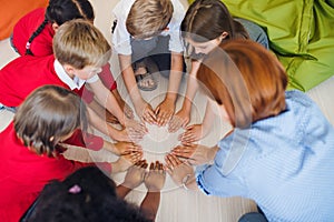 A top view of group of small school kids with teacher sitting on the floor in class.