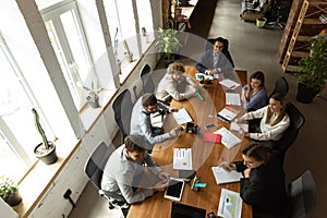 Top view of group of young people, co-workers during working process, meeting at office, indoors. Work, finance, tech