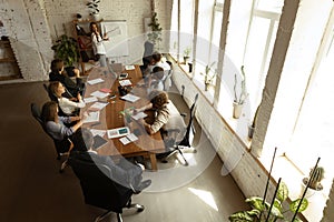 Top view of group of young people, co-workers during working process, meeting at office, indoors. Work, finance, tech