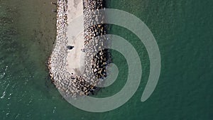 Top view of a groyne surrounded by rocks stretching into the sea. Tranquility of ocean waves meeting the structure