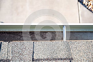 Top view of a gutter system on a residential house.  Asphalt shingles and support brackets visible