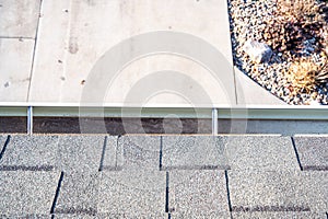 Top view of a gutter system on a residential house.  Asphalt shingles and support brackets visible