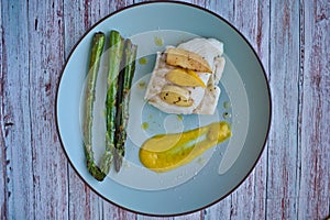 Top view of hake fillet with mango sauce and asparagus. Plate with warm colours and yellow background. Seafood dish