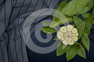 Top view of half a garlic bulb on bay leaves and a towel on a dark background