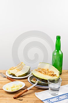 Top view of half green melon, plates with pieces, fork and knife on wooden table