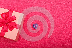 Top view of half of pink gift box on a Crimson backdrop and blue heart beside. Gift box in red ribbon with cold blue gems heart