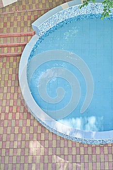 Top view of a half round outdoor swimming pool with blue mosaic ceramic tiles, with blue clear water. Background with