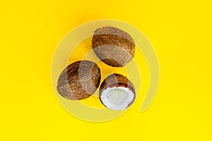 Top view half and two whole coconuts on a yellow background. Tropical summer mockup. Minimal flatlay. Natural ingredient