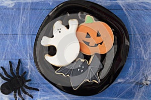 Top view of halloween biscuits on blue wooden table decorated with spider web and spiders