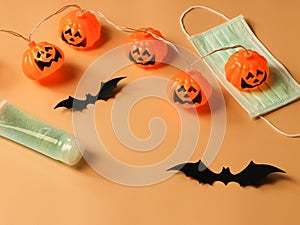 Halloween pumpkin lights , black paper bats,medical mask and alcohol sanitizer gel on orange background. Halloween , COVID-19