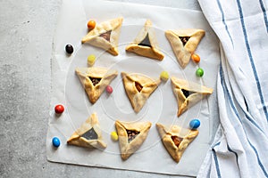 Top view hamantaschen cookies and colorful candies on a baking paper with napkin on a gray background