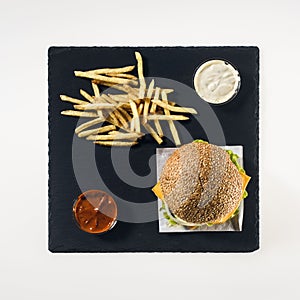 top view of hamburger, french fries and sauces on black stone board,