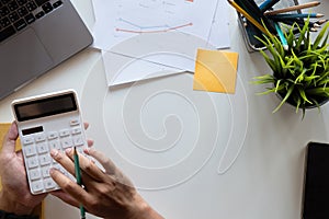 Top view hand of accountant using calculator on workplace with copy space, calculator and plant potted on white desk