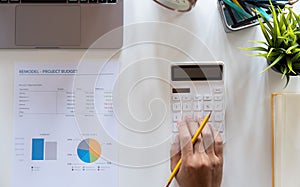 Top view hand of accountant using calculator on workplace with copy space, calculator and plant potted on white desk