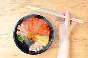 Top view of the hand  with chopsticks on a wooden table ready to eat Japanese Rice with Salmon and Tobiko