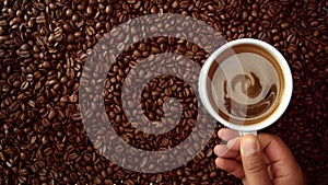 Top view of hand with cup of black coffe put it on coffe beans background