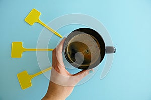 Top View of a Hand Holding a Black Cup of Coffee and Empty Yellow LAbels isolated on a BLue Background