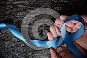 Top view of hand holding blue ribbon on wooden background with copy space. Men`s health and prostate cancer awareness and concept.
