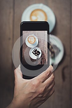 Top view of Hand holding mobile take a photo of coffee cup and c