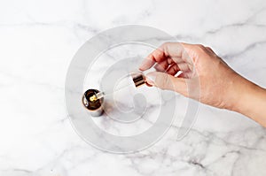 Top view of hand holding a retinol oil serum pipette and oil bottle on isolated marble background. Beauty care concept photo