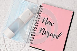 Top view of hand sanitizer, face mask and a notebook with "New Normal" text on a white puzzle photo