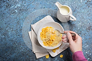 Tasty breakfast of sweet cornflakes in milk and hand with spoon