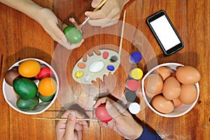 Top view of hands of family members are painting eggs with a paintbrush on wooden table for preparing Easter day. Happy family ti